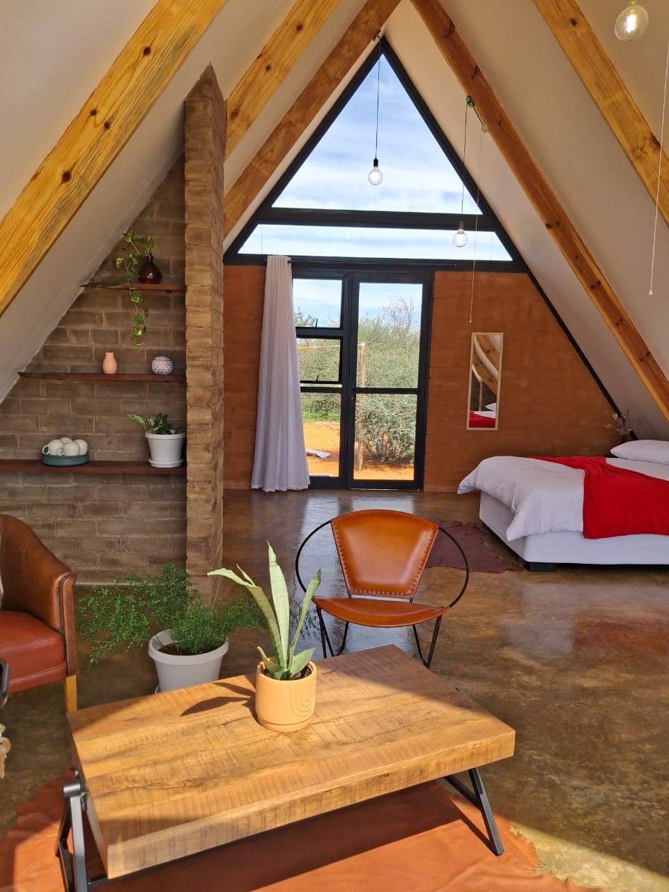 Cozy A-frame cabin interior featuring wooden beams, brick walls, and a large triangular window.