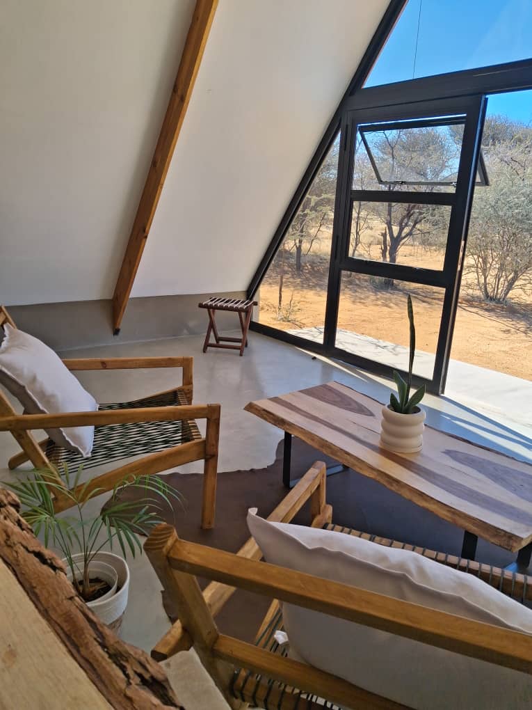 Modern A-frame cabin interior featuring wooden furniture and large windows overlooking a desert landscape.