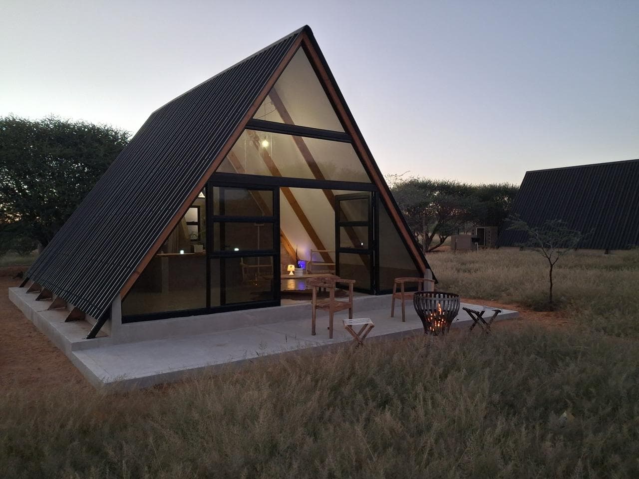Modern A-frame cabin with glass front and fire pit on a concrete patio at dusk.