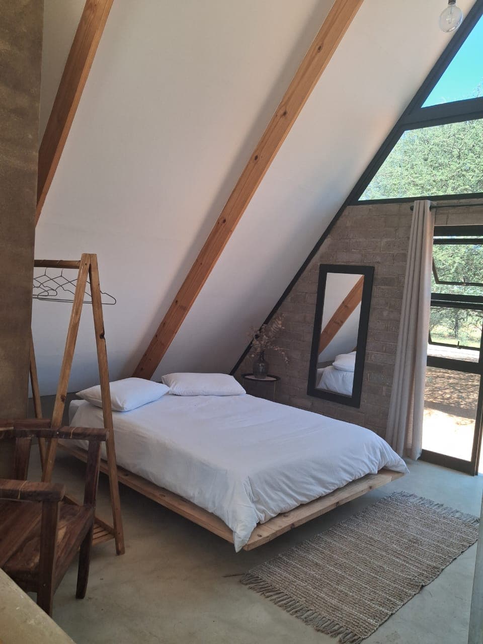 Minimalist A-frame bedroom featuring a wooden platform bed, white linens, and exposed timber beams.