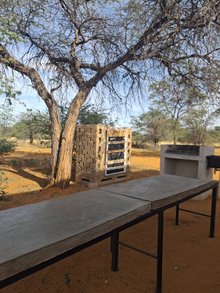 Outdoor cooking area with a concrete table, brick smoker, and grill in a sandy landscape.