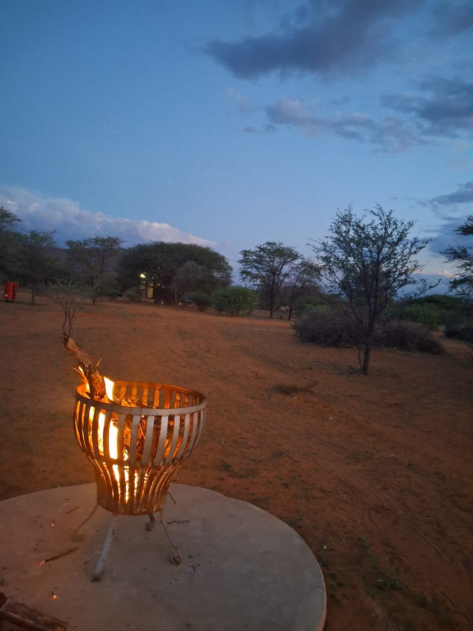 A metal fire basket glows with burning wood in a sandy landscape at twilight.