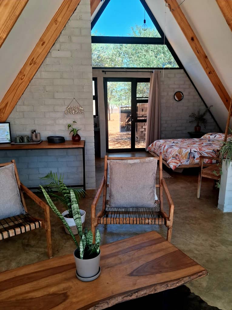 Cozy A-frame cabin interior featuring white brick walls, wooden beams, and rustic furniture with plants.