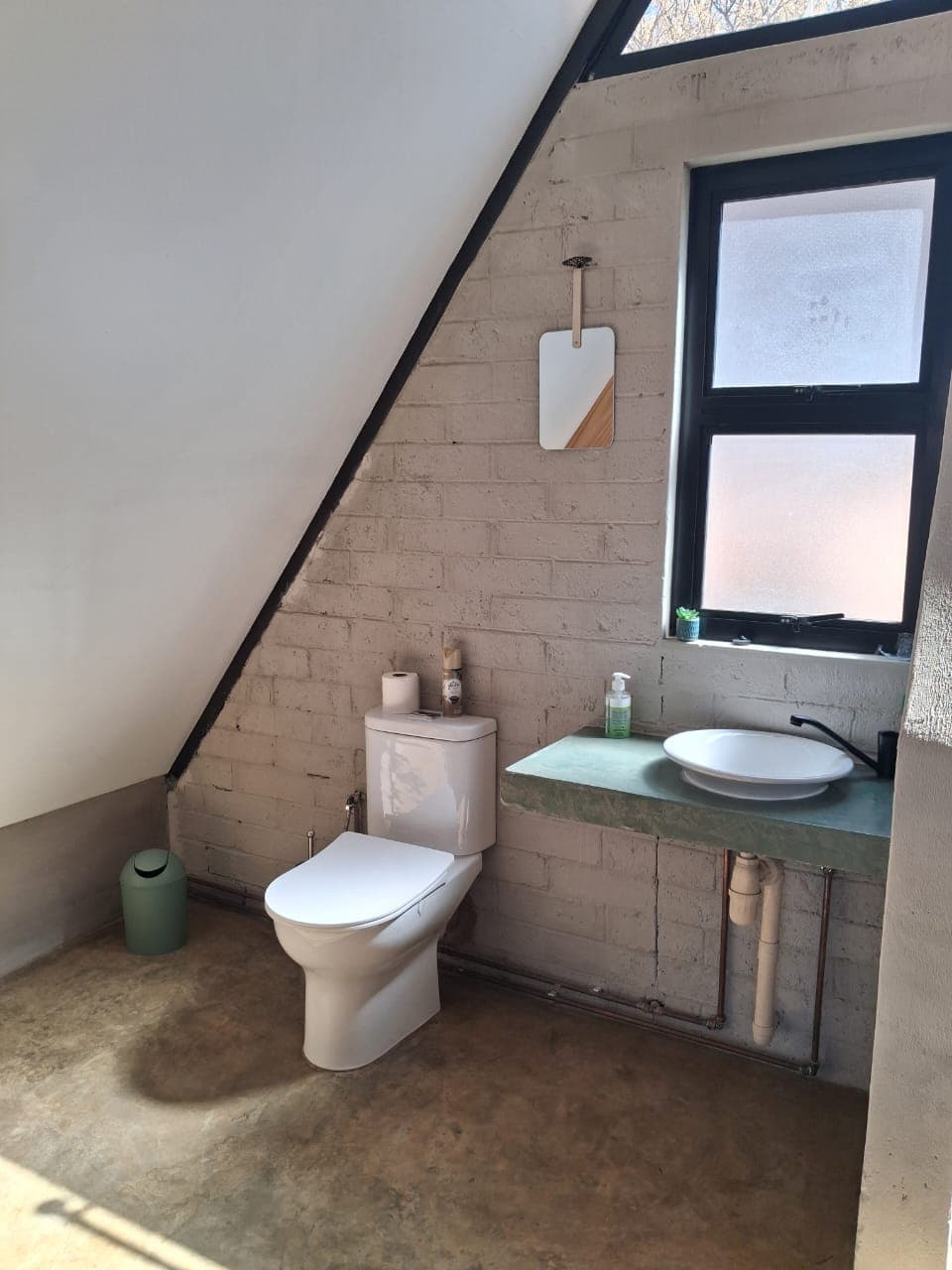 Minimalist bathroom featuring a white toilet and green floating vanity under a sloped ceiling.