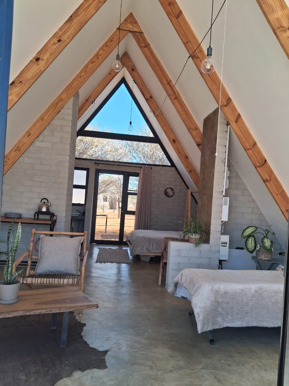 Modern A-frame cabin interior with exposed wooden beams, white brick walls, and large triangular window.